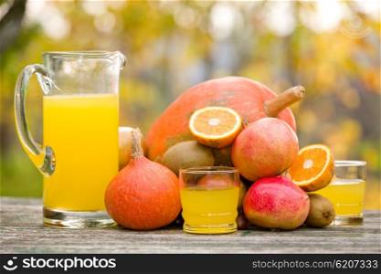 glasses of juice and lots of autumn fruits on wooden table, outdoor