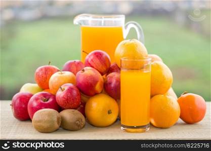 glasses of orange juice and lots of fruits on wooden table outdoor