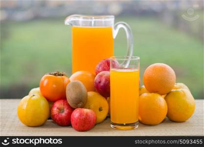 glasses of orange juice and lots of fruits on wooden table outdoor. orange juice
