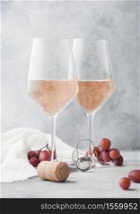 Glasses of pink rose homemade summer refreshing wine with corks, grapes and corkscrew on light table background.