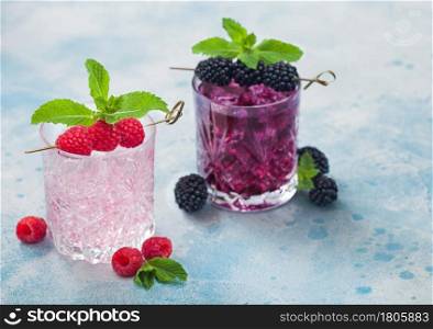 Glasses of pink soda lemonade and blackberry cocktail with ice cubes and mint on light blue background. Soda and alcohol mix.