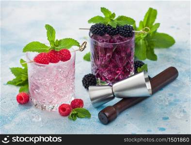 Glasses of pink soda lemonade and blackberry summer refreshing cocktail with ice cubes and mint on blue background with jigger and muddler