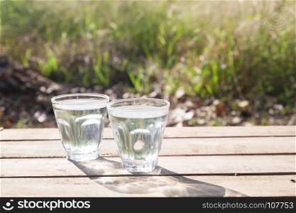 Glasses of pure water on wooden table with nature in background, Healthy lifestyle