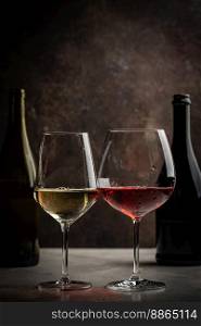 Glasses of red and white wine with bottles on dark rustic background. Glasses of red and white wine