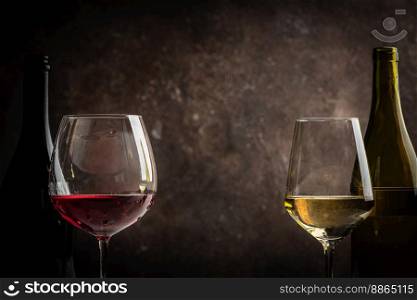 Glasses of red and white wine with bottles on dark rustic background. Glasses of red and white wine