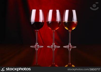 Glasses of red, rose and white wine over a draped background lit red
