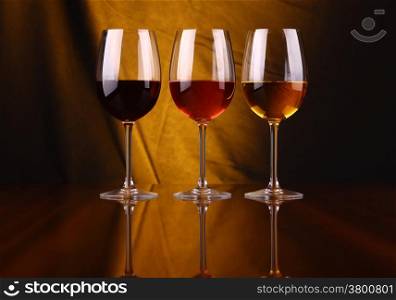 Glasses of red, rose and white wine over a draped background lit yellow