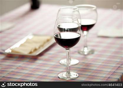 Glasses of red wine and cheese tray on a table with checkered tablecloth