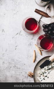 Glasses of red wine, cheese and grapes on rustic concrete background, copyspace, flat lay