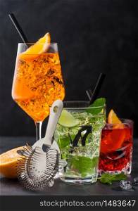 Glasses of spritz,mojito and negroni cocktails with ice cubes and lime and orange slices with mint leaf and black straw on dark background with strainer.
