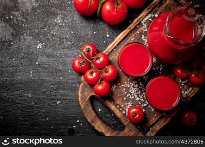 Glasses of tomato juice on a cutting board. On a black background. High quality photo. Glasses of tomato juice on a cutting board.