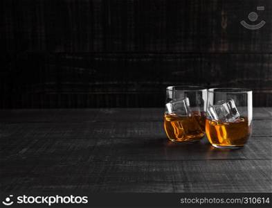 Glasses of whiskey with ice cubes on wooden background