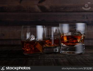 Glasses of whiskey with ice cubes on wooden table background