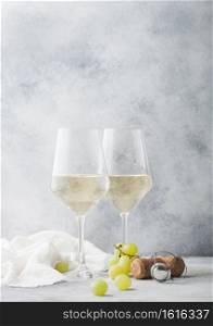 Glasses of white homemade summer refreshing wine with corks and grapes on light stone background.