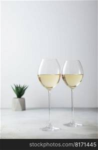 Glasses of white wine and small green flower on light board.