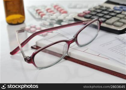 Glasses on banking report with calculator and pills in office
