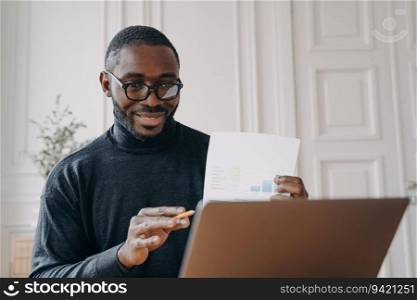 Glasses-wearing African American freelancer has remote video conference, holds financial report during online meeting.