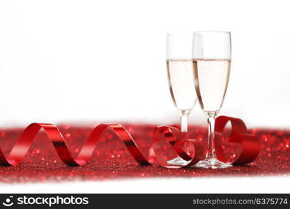 Glasses with Champagne and gifts on red glitters isolated on white background. Champagne on glitters