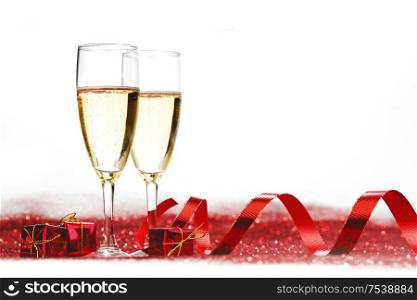 Glasses with Champagne and gifts on red glitters isolated on white background. Champagne on glitters