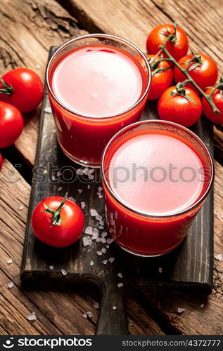 Glasses with tomato juice on a wooden cutting board. On a wooden background. High quality photo. Glasses with tomato juice on a wooden cutting board.