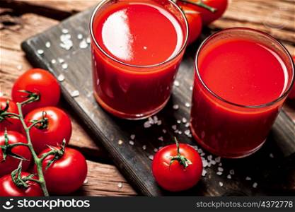Glasses with tomato juice on a wooden cutting board. On a wooden background. High quality photo. Glasses with tomato juice on a wooden cutting board.