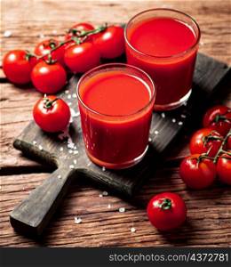 Glasses with tomato juice on a wooden cutting board. On a wooden background. High quality photo. Glasses with tomato juice on a wooden cutting board.