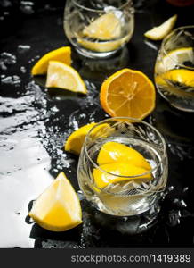 Glasses with vodka and lemon. On a black wooden background.. Glasses with vodka and lemon.