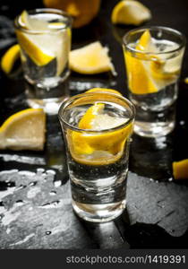 Glasses with vodka and lemon. On a black wooden background.. Glasses with vodka and lemon.