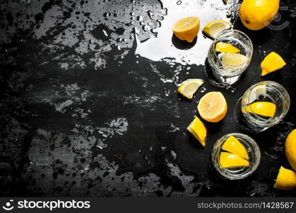 Glasses with vodka and lemon. On a black wooden background.. Glasses with vodka and lemon.