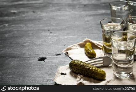 Glasses with vodka and pickled cucumbers on the old fabric. On a black wooden background.. Glasses with vodka and pickled cucumbers on the old fabric.