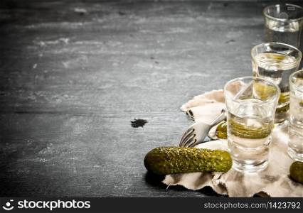 Glasses with vodka and pickled cucumbers on the old fabric. On a black wooden background.. Glasses with vodka and pickled cucumbers on the old fabric.