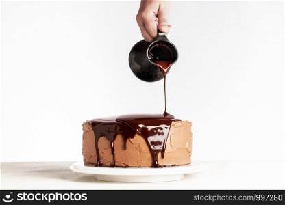 Glazing chocolate cake with melted chocolate. Woman pouring chocolate over cake. Homemade cocoa layered cake. Birthday cake and dripping chocolate.