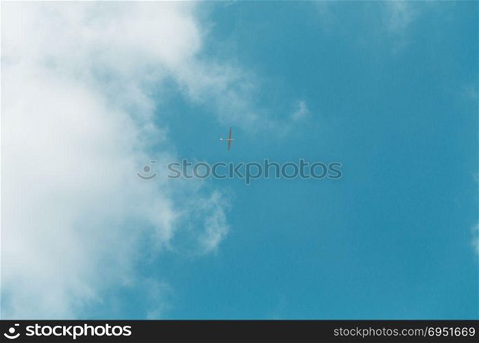 Glider gliding in blue sky from below.