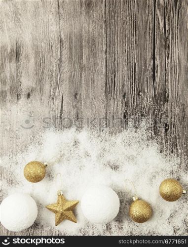Glittering gold Christmas balls, snowballs, winter snow and star on wooden background.