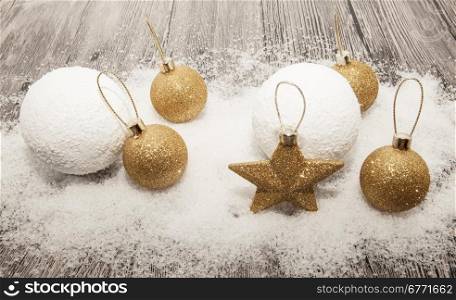 Glittering gold Christmas balls, snowballs, winter snow and star on wooden background.