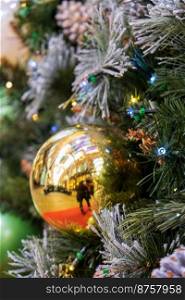 Glittery golden ball ornament hangs from bough of a Christmas tree. Christmas and New Year concept.