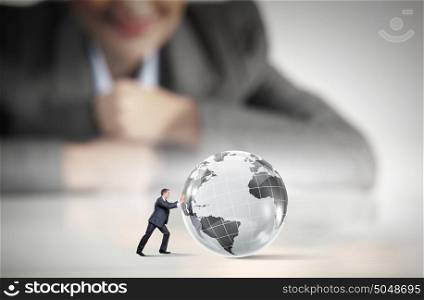 Global business. Businesswoman looking at miniature of man rolling Earth planet