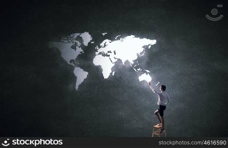Global business interaction. Rear vew of businesswoman climbing chair and touching world map on wall