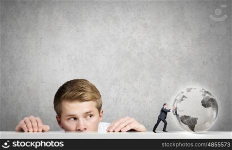 Global technologies. Young man looking out from under the table at businessman