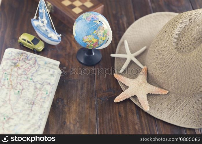 globe, hat, map, car ship and starfish figurine on wooden table for use as traveling concept (vintage tone and selected focus)