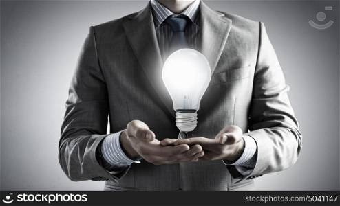 Glowing bulb in hands. Close up of businessman hands holding glass light bulb