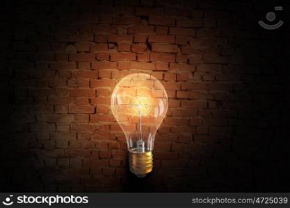 Glowing bulb on brick surface. One turned on light bulb on brick wall background