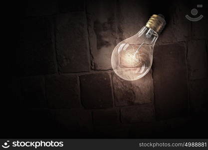 Glowing bulb on brick surface. One turned on light bulb on brick wall background