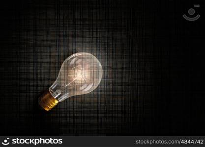 Glowing bulb on stone surface. One turned on light bulb on stone wall background