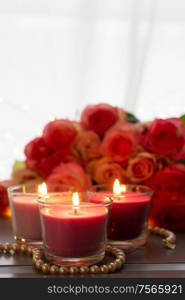 Glowing candles with rose fresh flowers bouquet on gray table, close up home interior details. fresh rose flowers on gray