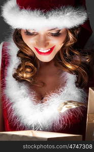 Glowing Christmas gift. Beautiful woman in Santa Claus style costume looking into glowing Christmas gift box