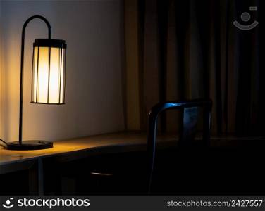 Glowing desk lamp on wooden table in the dark bedroom