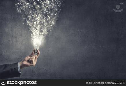 Glowing electric bulb . Hand holding glass glowing lightbulb on cement background