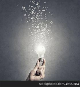Glowing electric bulb . Hand holding glass glowing lightbulb on cement background