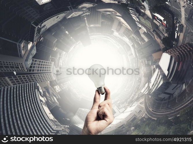 Glowing electric bulb . Hand holding glass glowing lightbulb on city background